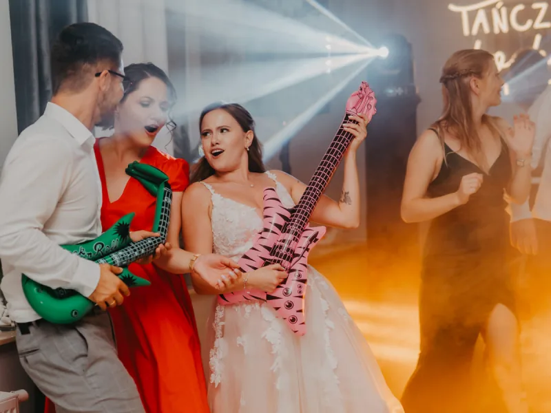 Panna młoda i goście grają na dmuchanych gitarach w dymie
