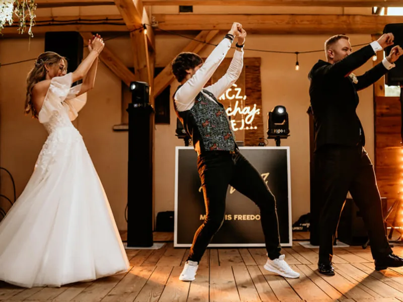 Wodzirej tańczy z parą młodą przed konsolą DJ-a