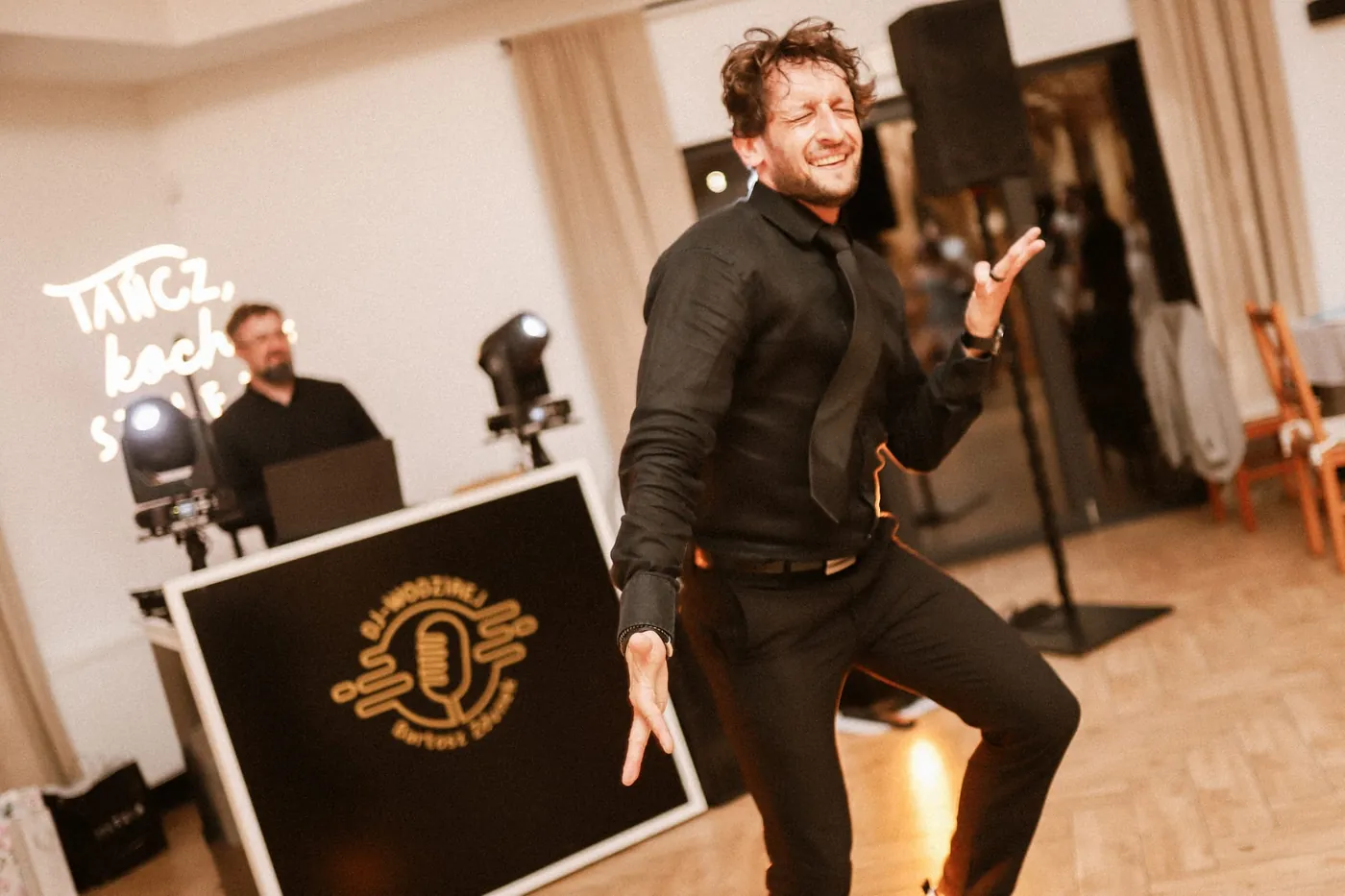 Roześmiany wodzirej tańczy przed konsolą z logo DJ / Wodzirej Bartosz Zdunek